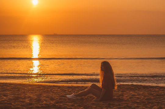 Young blonde girl in red dress sitting in the evening on the beach