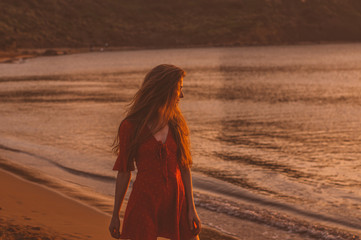 Young blonde girl in red dress staying in the evening on the beach