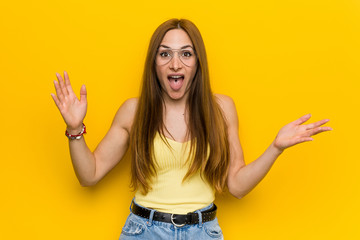 Young redhead ginger woman with freckless receiving a pleasant surprise, excited and raising hands.