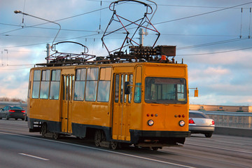 old yellow tram with two pantographs rides over the bridge