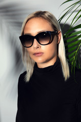 Naklejka premium Close-up of woman with sunglasses hiding behind tropical palm leaves