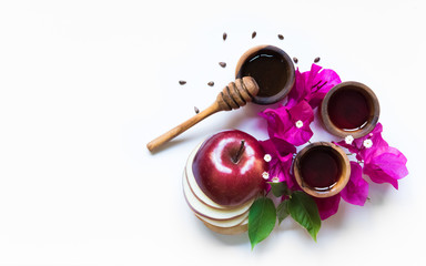 Rosh Hashanah Jewish holiday concept - red apple with slices, wooden dipper, saucer of honey on white background with pink flowers. Traditional holiday symbols