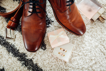 Groom's wedding day accessories. Brown leather shoes, belt, perfume, golden rings. Male fashion