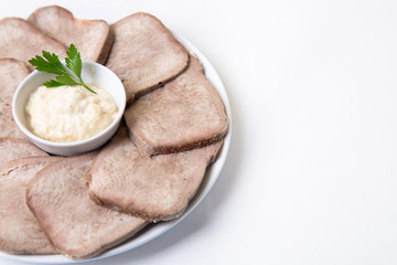 Beef boiled tongue with horseradish on a white plate. White background, isolated. Place for text. Close-up.
