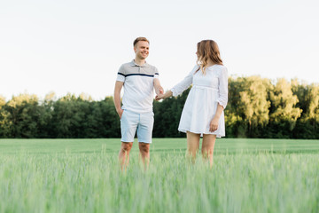 Young pretty couple in love standing in the field. Handsome cheerful blonde girl in white dress hugging her boyfriend. Man and woman having fun outdoors