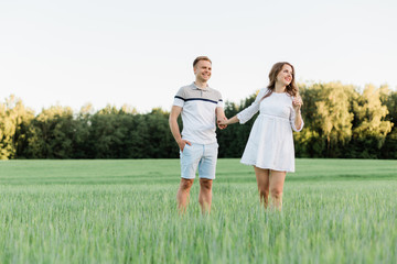 Young pretty couple in love standing in the field. Handsome cheerful blonde girl in white dress hugging her boyfriend. Man and woman having fun outdoors