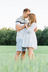 Obraz premium Young pretty couple in love standing in the field. Handsome cheerful blonde girl in white dress hugging her boyfriend. Man and woman having fun outdoors