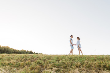 Naklejka premium Young pretty couple in love standing in the field. Handsome cheerful blonde girl in white dress hugging her boyfriend. Man and woman having fun outdoors