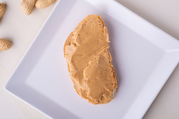 Peanut butter bread sandwich on white square shaped plate peanuts nut wooden background