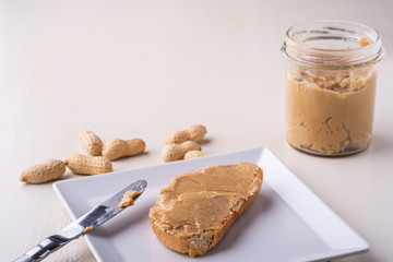 Peanut butter bread sandwich on white square shaped plate peanuts nut table knife wooden background