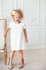 Little pretty girl in white dress trying on mummy's shoes