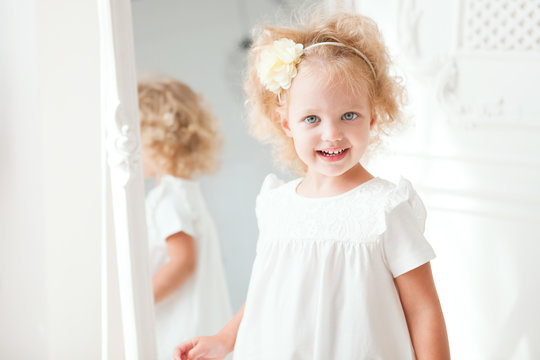 Portrait Little pretty smiling girl in white dress playing in white room