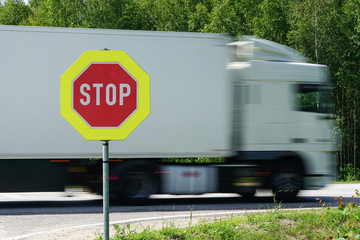 red stop road sign in the foreground and blurred fast truck in the background