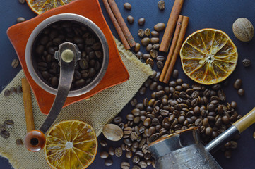 Coffee beans and a manual coffee grinder on a dark blue background, with cinnamon sticks and orange slices