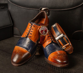 Classic men's shoes, trouser belt and expensive watches lie on the leather of python against the background of men's leather briefcases