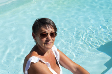 femme brune de 70 ans au bord de la piscine