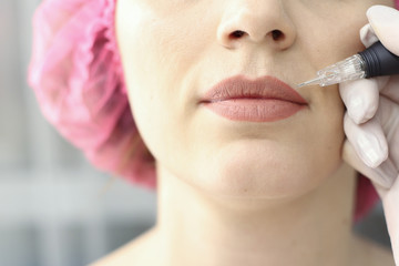 Young woman having permanent makeup on lips in beautician salon