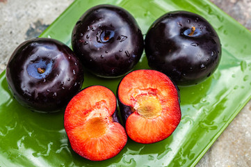 Three dark purple plum fruits and one cut on a green plate