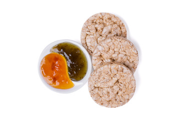 Round whole grain cereal crispbreads with peach and gooseberry jam in white sauce dish. Cutout, top view