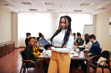 Face of handsome african business woman, holding tablet on the background of business peoples multiracial team meeting, sitting in office table.