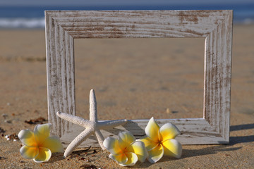 Photo frame on sand with starfish and flowers 