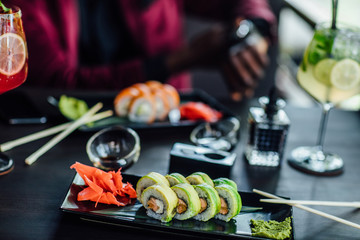 Man is eating sushi in the black plate on a wooden table. Rolls close-up.