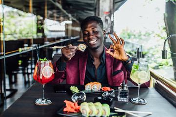 Portrait of african man  holding chopsticks sushi rolls. Okay sign.
