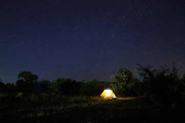 Camping tent under beautiful night sky full of stars. Starry night sky above illuminated touristic tent.