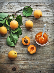 Apricot jam in jar on wooden table and fresh apricots on background. Overhead shot.