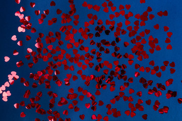 Sparkling and holographic red hearts on deep blue background. Festive concept. A photo in low key