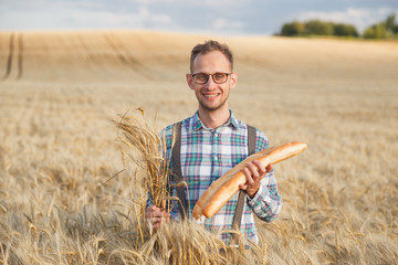 Naklejka na ściany i meble Happy farmer hold bakery products and ears of corn standing in ripe wheat field.