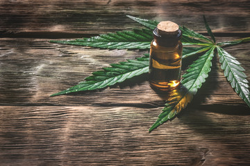 Cannabis essential oil in the vial with a green leaf on a wooden table background with a copy...