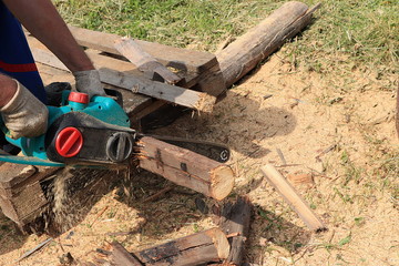 Fototapeta premium Preparation of firewood for the winter in the village, working saw and male hands in close-up. Electric saw and firewood in summer,