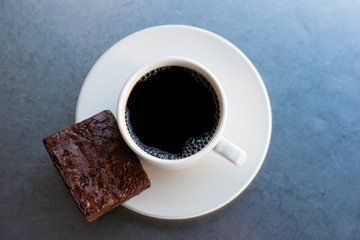 Black Coffee in White Cup on Saucer on metal table outside with brownie dessert with reflections and steam