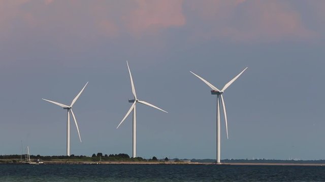 Three windmills are spinning while airplane is flying in background
