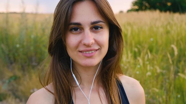 Happy young woman use smartphone and headphone standing in field at sunset, healthy lifestyle. Sportywoman runner using smartphone outdoor.
