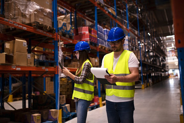 Coworkers working together in warehouse distribution storage area checking inventory. Warehouse...