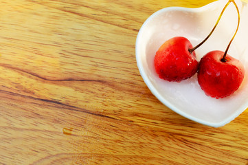 background with two cherries and white heart shaped bowl on a wooden table, copy space for text