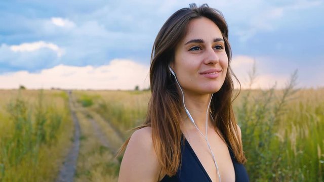 Happy young woman use smartphone and headphone standing in field at sunset, healthy lifestyle. Sportywoman runner using smartphone outdoor.