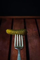 CUCUMBER PINCHED IN FORK ON WOODEN TABLE AND DARK BACKGROUND