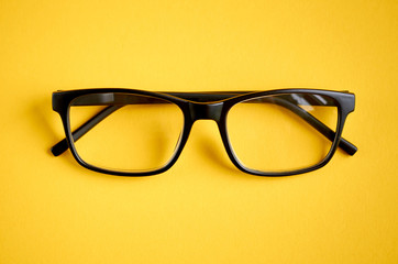 Black glasses on yellow background composition, eyeglasses.