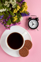 Coffee cup with cookies, alarm clock, flowers, on pink background composition.