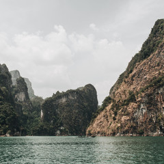 Exotic and tropical dark green and brown islands with rocks and green lake at Cheow Lan Lake, Khao...