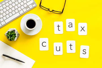 work desk with tax cuts text, keyboard, coffee and notebook on yellow background top view
