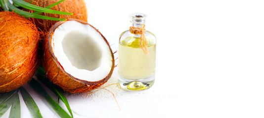 Coconut palm oil in a bottle with coconuts and green palm tree leaf on white background. Coco nut closeup. Healthy food, skincare concept