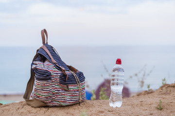 Water bottle and light backpack on the dried ground against the background of the sea, the ocean.