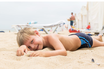 A little boy is lying on the sand in the summer. Rest of the child on the beach. © Konstiantyn Zap