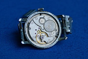one old gray clock with an open mechanism lies on a blue table