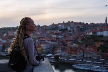 Young woman standing with camera in old town during dusk, Porto, Portugal. Tourism and travel.