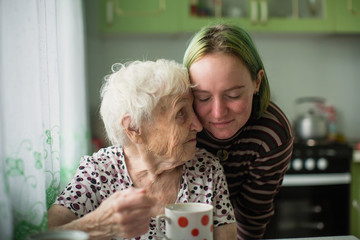 Portrait of elderly woman with her granddaughter at the table in the kitchen at home.